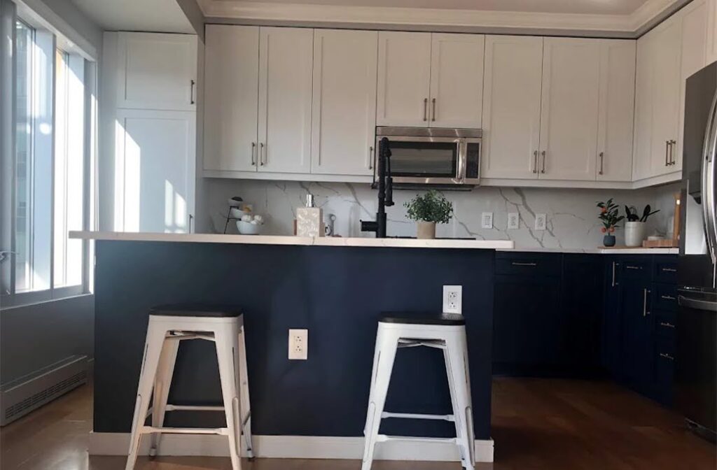 Bright kitchen with white upper cabinets, dark blue lower cabinets and island, white countertops, and wood floors.
