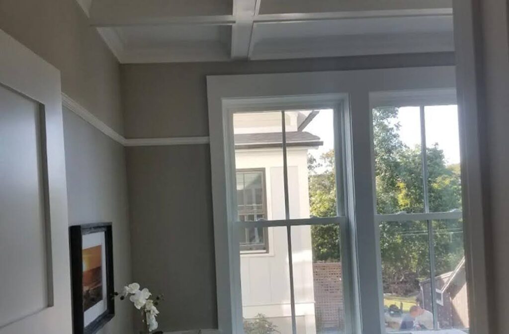 Finished home office with gray walls, white trim, coffered ceiling, and two large windows.